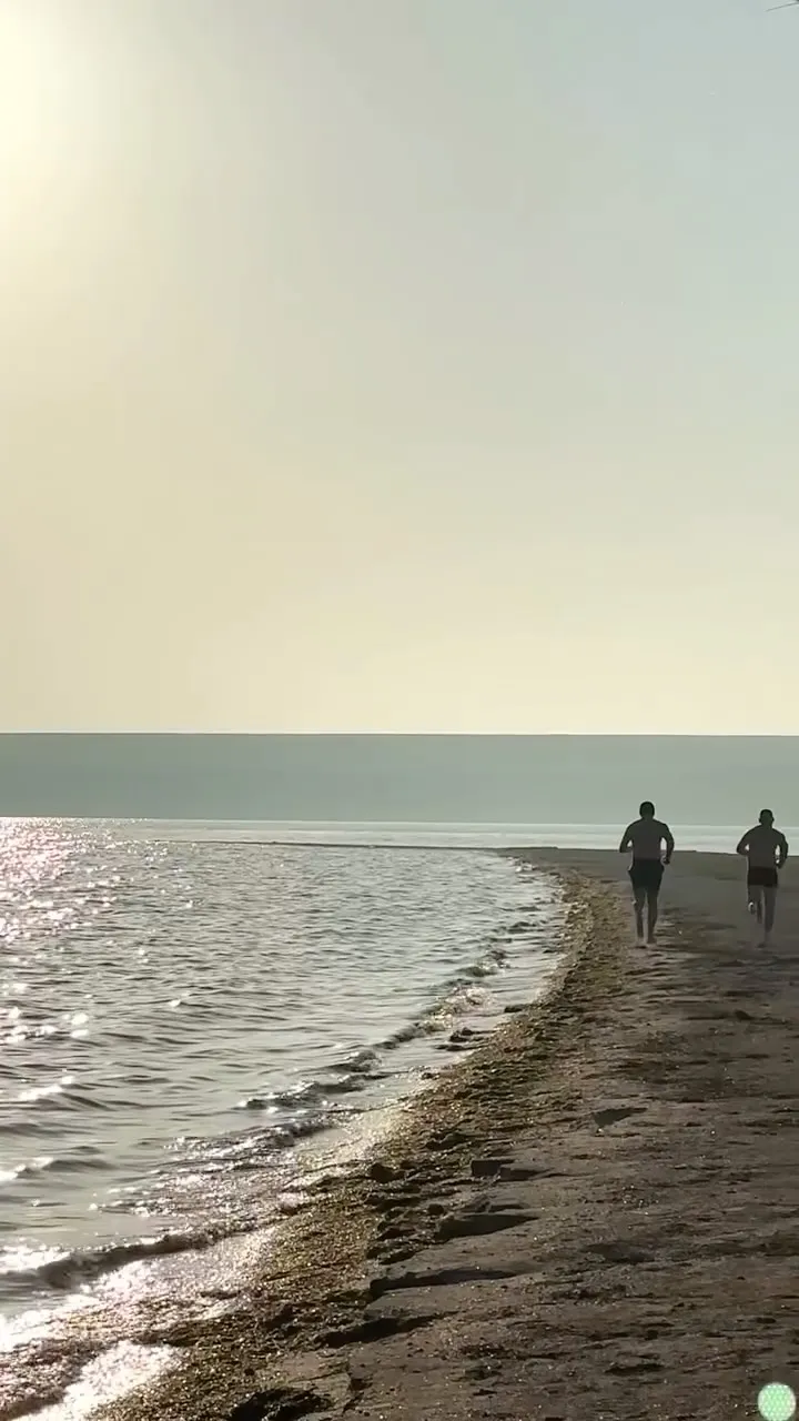 Двоє чоловіків біжать берегом косі на світанку